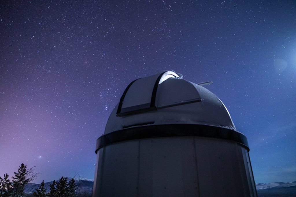 A telescope is silhouetted against a starry night sky