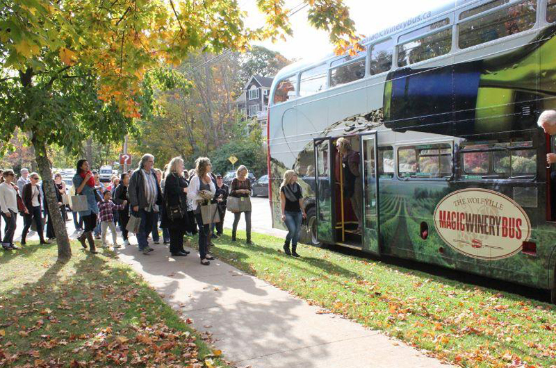 A group of people walk towards a double decker bus near a tree