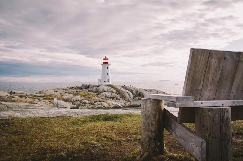 A lighthouse sits on a rocky hill, with the edge of a wooden bench in the foreground