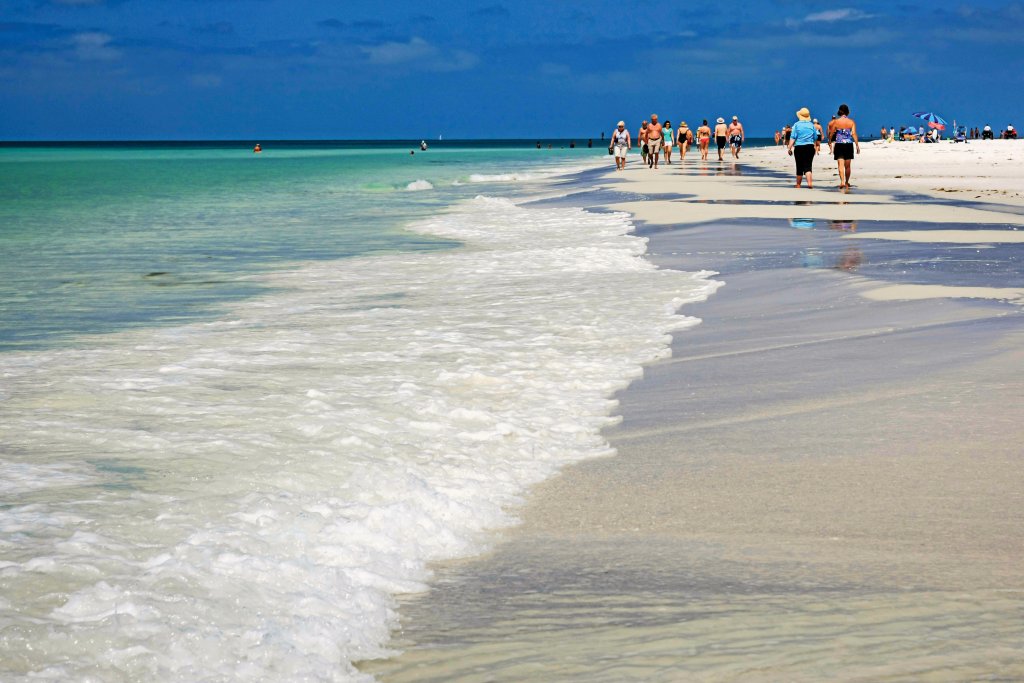 Beachgoers walk along white sands next to turquoise ocean