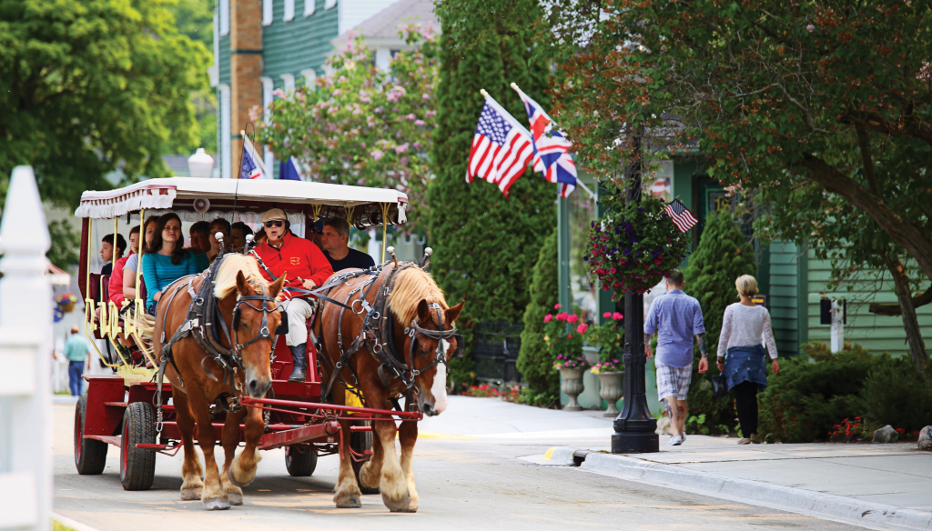 Tourists sit in a carriage pulled by two horses along a picturesque street.