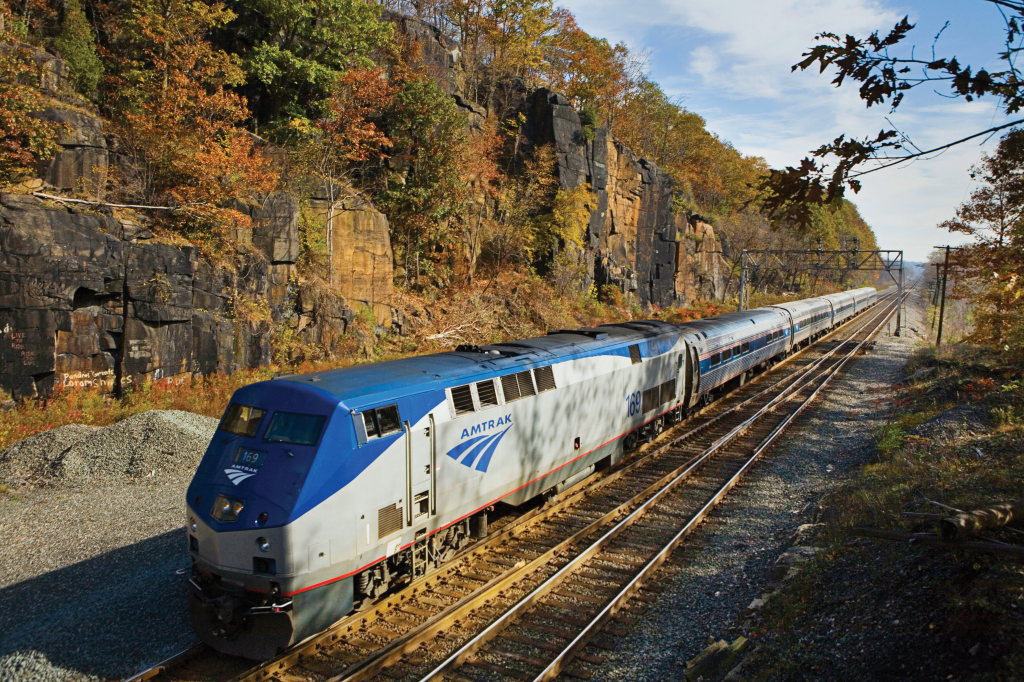Amtrak train passes through a sunlit mountainous region.