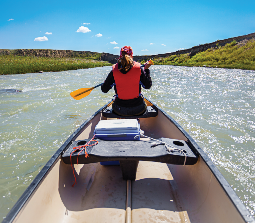 A woman sits in the bow of a canoe, paddling.