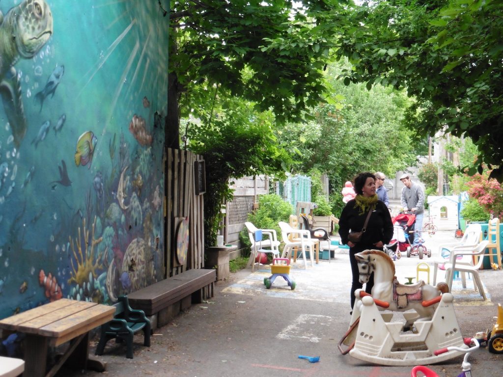 A woman strolls down a green alley, two walk with a stroller in the background